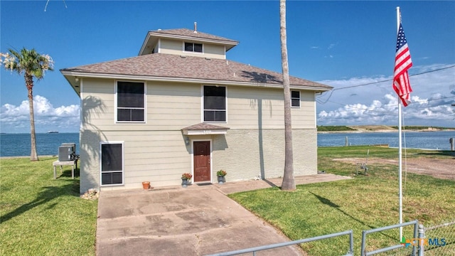 front facade featuring central AC unit, a patio area, a water view, and a front yard