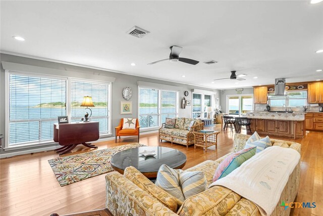 living room with ceiling fan, light wood-type flooring, and crown molding