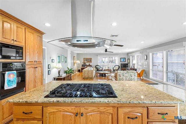 kitchen featuring island exhaust hood, black appliances, a healthy amount of sunlight, and light stone counters