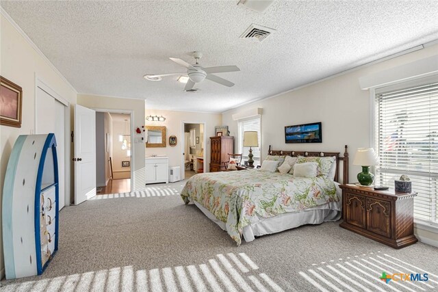 bedroom with a textured ceiling, light colored carpet, ceiling fan, and ensuite bath