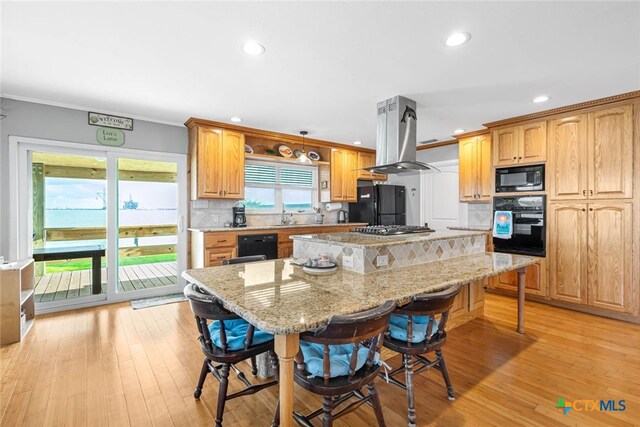 kitchen with light hardwood / wood-style floors, island range hood, a center island, black appliances, and backsplash