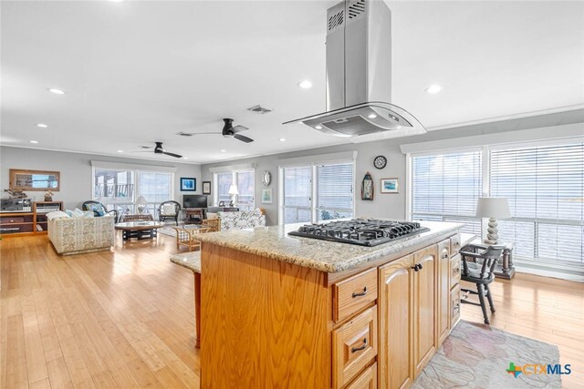 kitchen featuring light hardwood / wood-style floors, stainless steel gas cooktop, island range hood, and a breakfast bar area