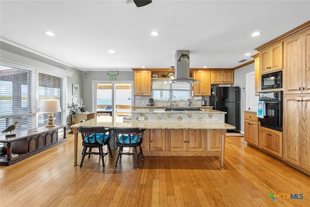 kitchen featuring light stone counters, black appliances, island exhaust hood, a kitchen island, and light hardwood / wood-style flooring