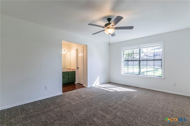 unfurnished bedroom with ensuite bath, ceiling fan, and dark carpet