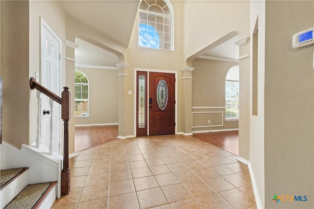 foyer entrance with decorative columns, light tile patterned flooring, a towering ceiling, and a wealth of natural light