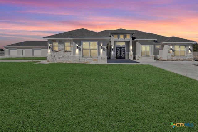 prairie-style house with stucco siding, a lawn, stone siding, french doors, and concrete driveway