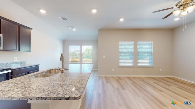 kitchen featuring light stone counters, a sink, visible vents, light wood-style floors, and dark brown cabinets