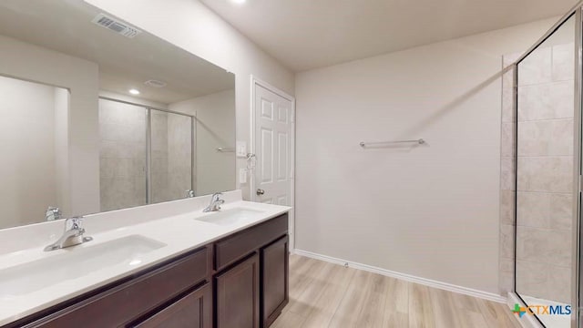 bathroom featuring a tile shower, wood finished floors, a sink, and visible vents