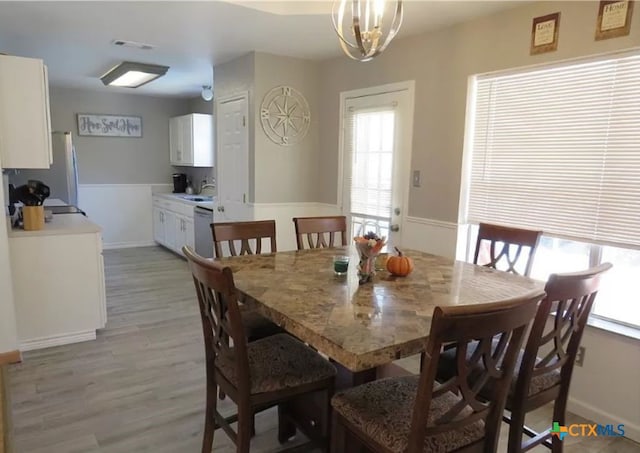 dining space featuring light wood-type flooring, sink, and a notable chandelier