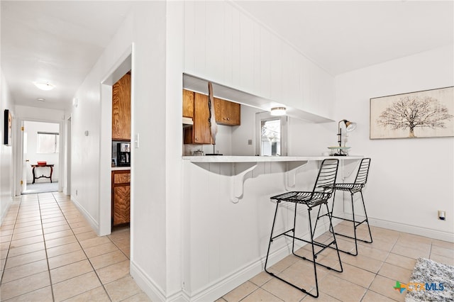 kitchen featuring a breakfast bar area, light tile patterned floors, and kitchen peninsula