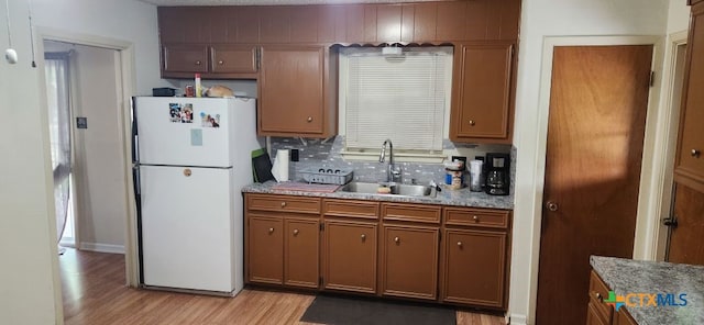 kitchen with white refrigerator, sink, backsplash, light stone countertops, and light wood-type flooring