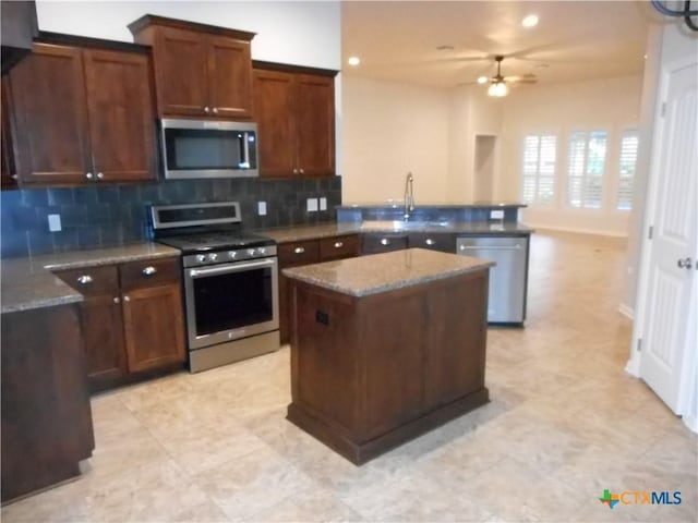 kitchen featuring appliances with stainless steel finishes, backsplash, dark stone counters, a kitchen island, and sink