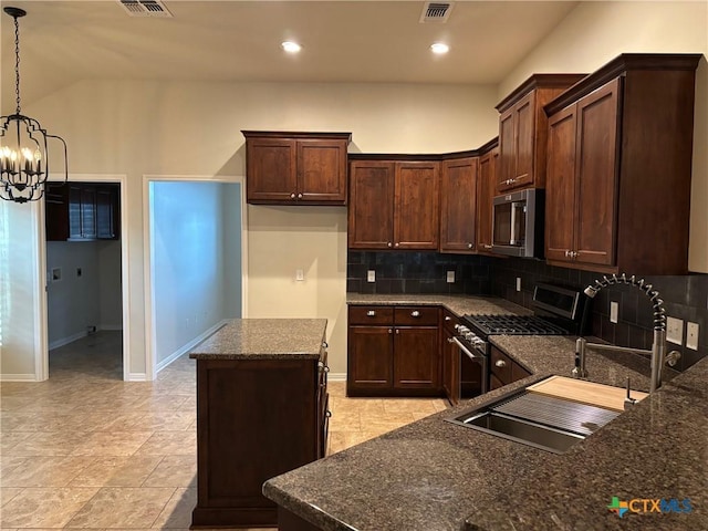 kitchen featuring dark stone countertops, backsplash, hanging light fixtures, a notable chandelier, and gas range