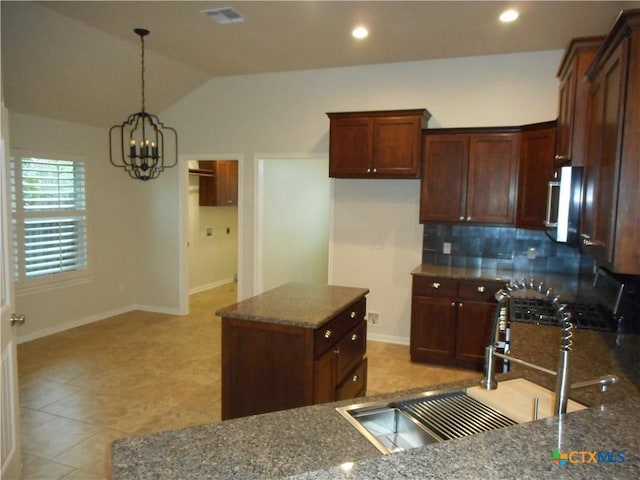 kitchen featuring lofted ceiling, a kitchen island, dark stone countertops, sink, and a chandelier