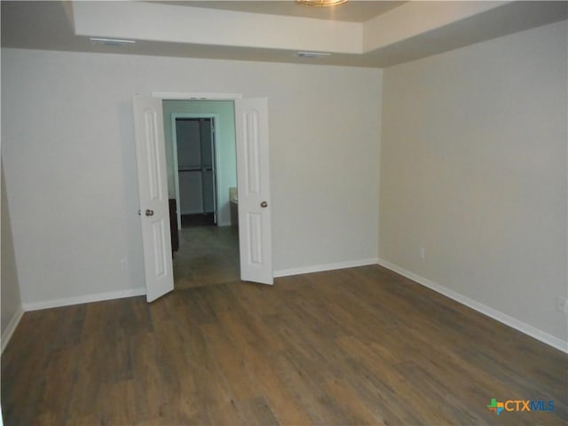 empty room with dark hardwood / wood-style floors and a tray ceiling