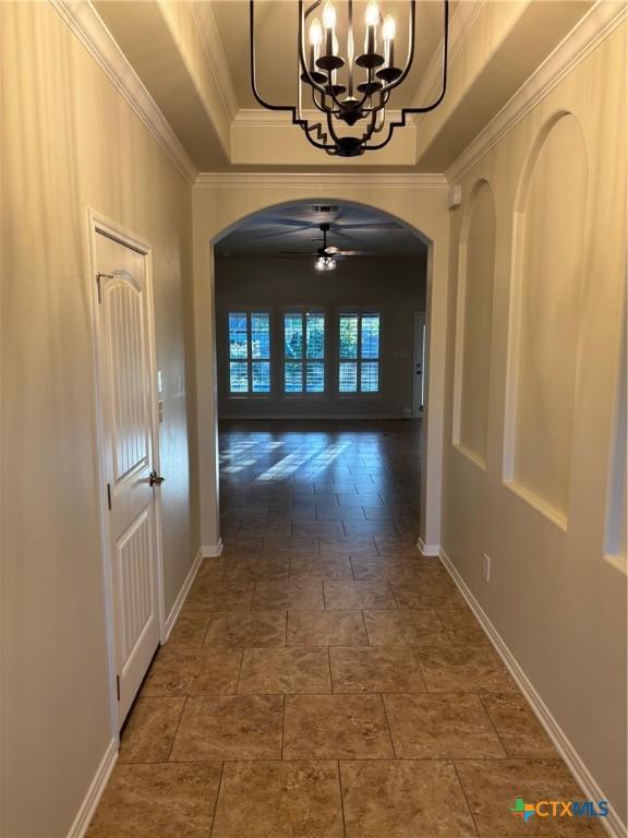 hallway with ornamental molding, a chandelier, and a tray ceiling