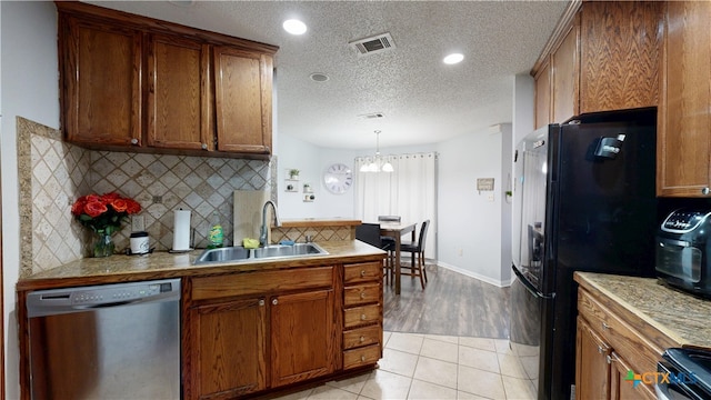 kitchen with brown cabinetry, stainless steel dishwasher, visible vents, and a sink