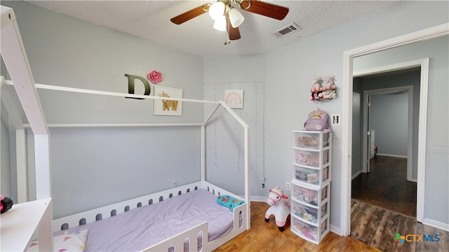 bedroom featuring wood finished floors, visible vents, a textured ceiling, and a ceiling fan