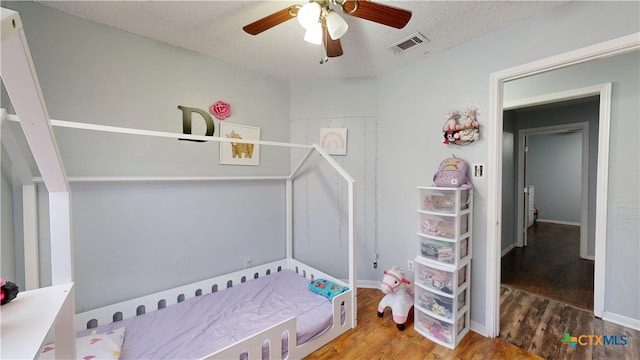 bedroom with a textured ceiling, wood finished floors, visible vents, baseboards, and a ceiling fan