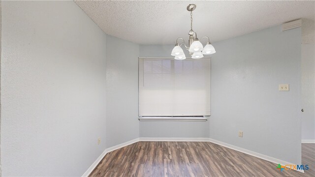 spare room featuring baseboards, wood finished floors, a textured ceiling, and a notable chandelier