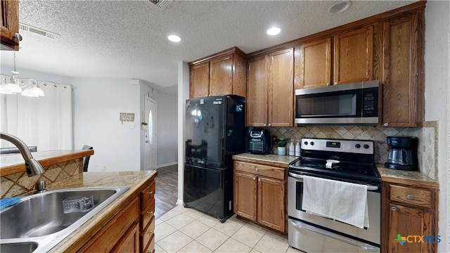 kitchen with brown cabinetry, decorative backsplash, stainless steel appliances, and a sink