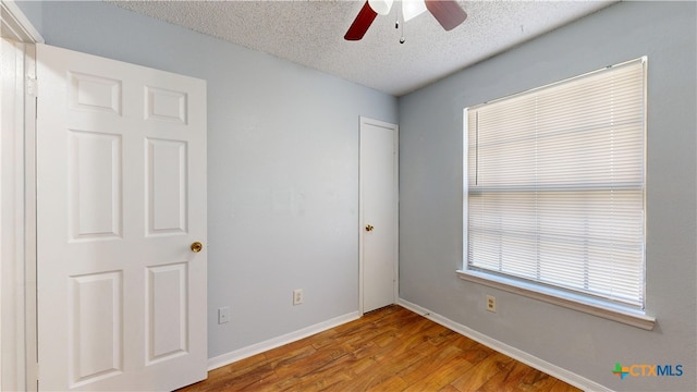 unfurnished bedroom with wood finished floors, a textured ceiling, baseboards, and ceiling fan