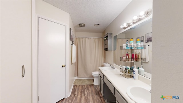 full bathroom with double vanity, a textured ceiling, a sink, and wood finished floors