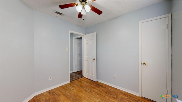 unfurnished bedroom featuring a textured ceiling, light wood-type flooring, baseboards, visible vents, and a ceiling fan