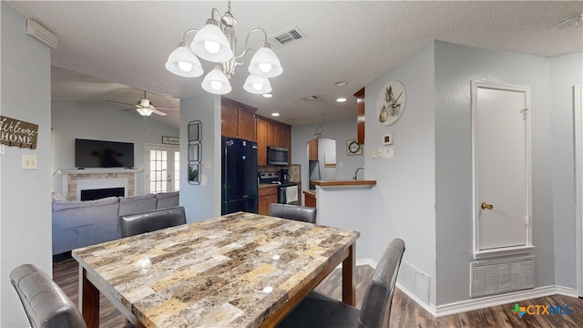 dining space featuring a textured ceiling, dark wood-style flooring, visible vents, ceiling fan with notable chandelier, and a fireplace