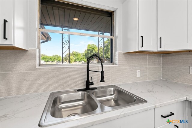 kitchen featuring white cabinetry, sink, light stone counters, and tasteful backsplash