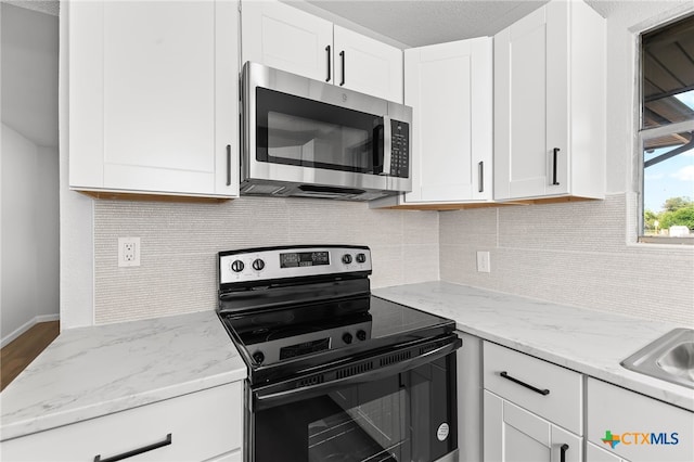 kitchen with light stone counters, white cabinets, hardwood / wood-style floors, tasteful backsplash, and black range with electric cooktop