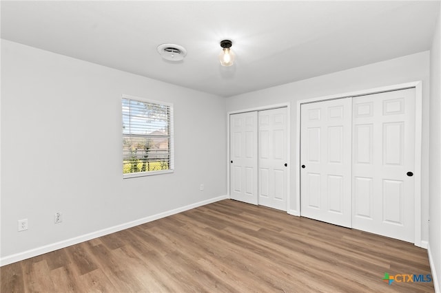 unfurnished bedroom with multiple closets and hardwood / wood-style floors