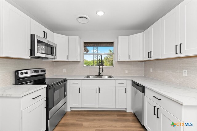 kitchen featuring white cabinets, wood-type flooring, light stone counters, and appliances with stainless steel finishes