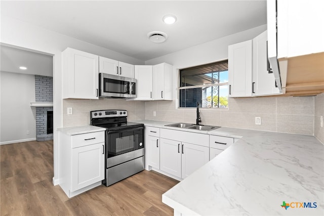 kitchen with stainless steel appliances, white cabinets, sink, and light hardwood / wood-style flooring