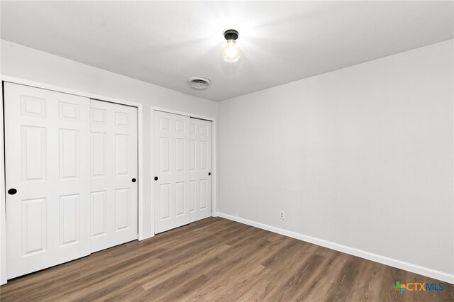 unfurnished bedroom featuring multiple closets and dark hardwood / wood-style floors