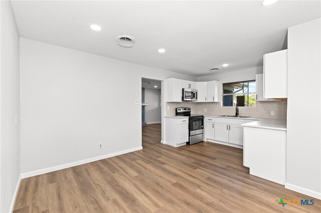 kitchen with white cabinets, hardwood / wood-style flooring, tasteful backsplash, sink, and appliances with stainless steel finishes