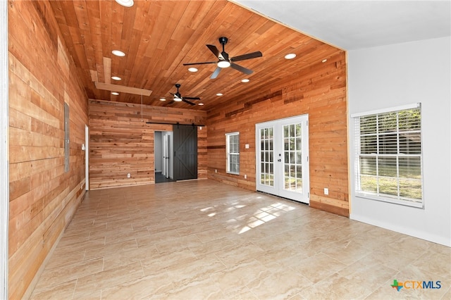 empty room with a barn door, wooden ceiling, ceiling fan, and wooden walls