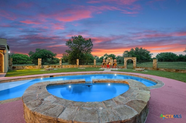 pool at dusk with an in ground hot tub and a fireplace