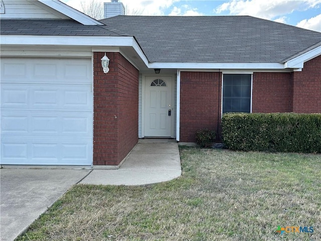 entrance to property featuring a yard, brick siding, a chimney, and an attached garage