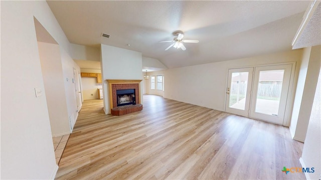 unfurnished living room featuring visible vents, a ceiling fan, light wood-style flooring, vaulted ceiling, and a brick fireplace