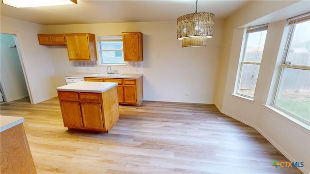 kitchen with brown cabinetry, a sink, light countertops, light wood-type flooring, and a wealth of natural light