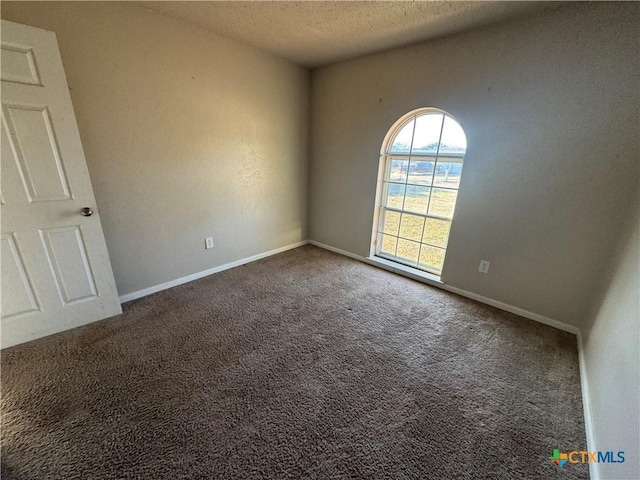 spare room featuring dark carpet and a textured ceiling