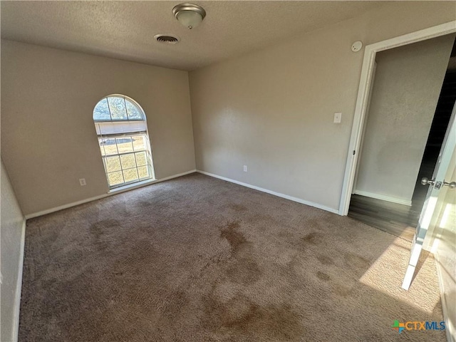 spare room with a textured ceiling and dark carpet