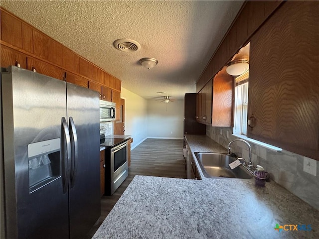 kitchen featuring appliances with stainless steel finishes, a textured ceiling, decorative backsplash, sink, and ceiling fan