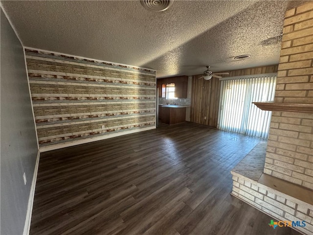 unfurnished living room featuring ceiling fan, dark wood-type flooring, a textured ceiling, and wooden walls