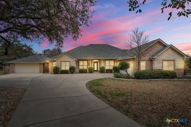 ranch-style home with driveway, stone siding, an attached garage, and brick siding