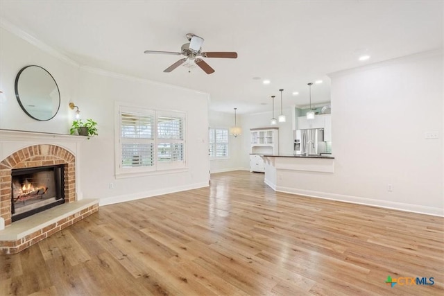 unfurnished living room featuring crown molding, light wood-style floors, a brick fireplace, ceiling fan, and baseboards