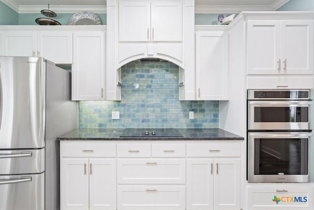 kitchen with white cabinets, ornamental molding, appliances with stainless steel finishes, backsplash, and dark stone counters