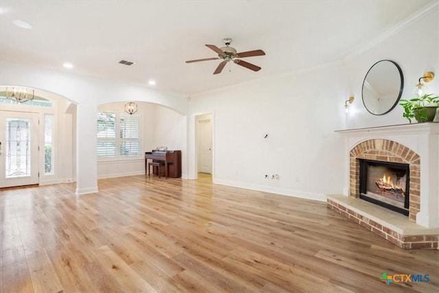 unfurnished living room featuring ceiling fan with notable chandelier, a fireplace, baseboards, light wood-style floors, and ornamental molding