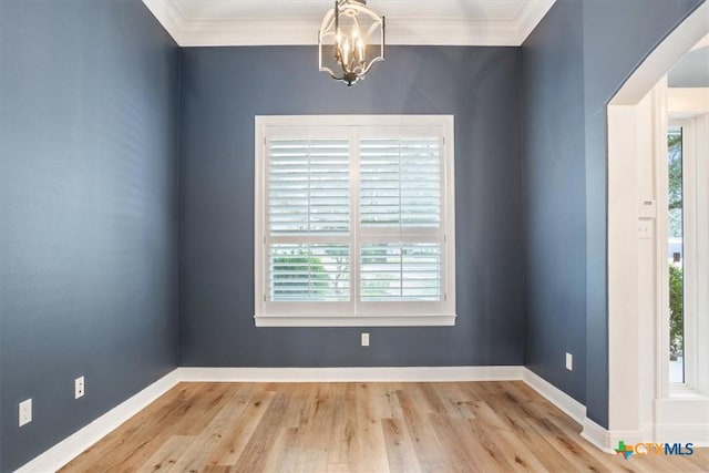 spare room featuring baseboards, arched walkways, light wood-style flooring, and crown molding